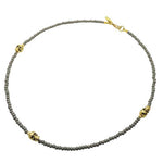 A men's grey glass beaded necklace with three gold skull charms adorned with gold stardust beads. by Dana Levy