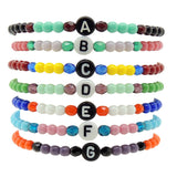 A Stack of Dana Levy Initial Letter Charm Glass Bead Mix Bracelets with the Letters A to G in a Variety of Colours.