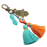 Dana Levy Mano Fico Hamsa Hand Evil Eye Trio Charm Tassel Bag Charm with a Turquoise Mano Fico, Antique Gold Hamsa Hand and Orange Evil Eye Charms. 