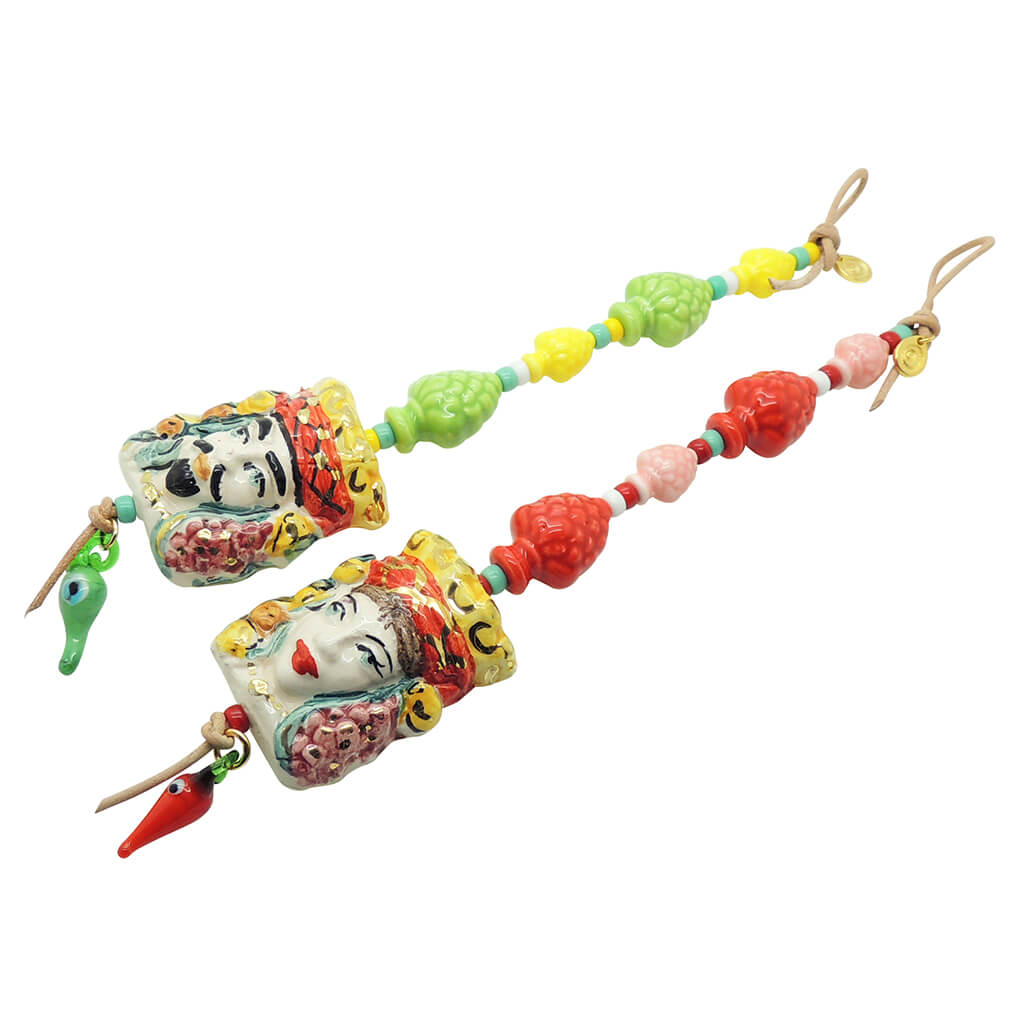 Dana Levy Sicilian Testa di Moro Charm Wall Hangings Duo - male moor head with green and yellow pine cones and a green evil eye chilli charm, and a female head with red and pink pines cones and a red evil eye chilli. 
