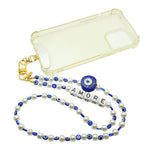 Dana Levy clear phone case with gold clip and metal phone strap card, faux pearl personalised phone strap with AMORE alphabet cube beads, and royal blue evil eye charm and beads on a white background.