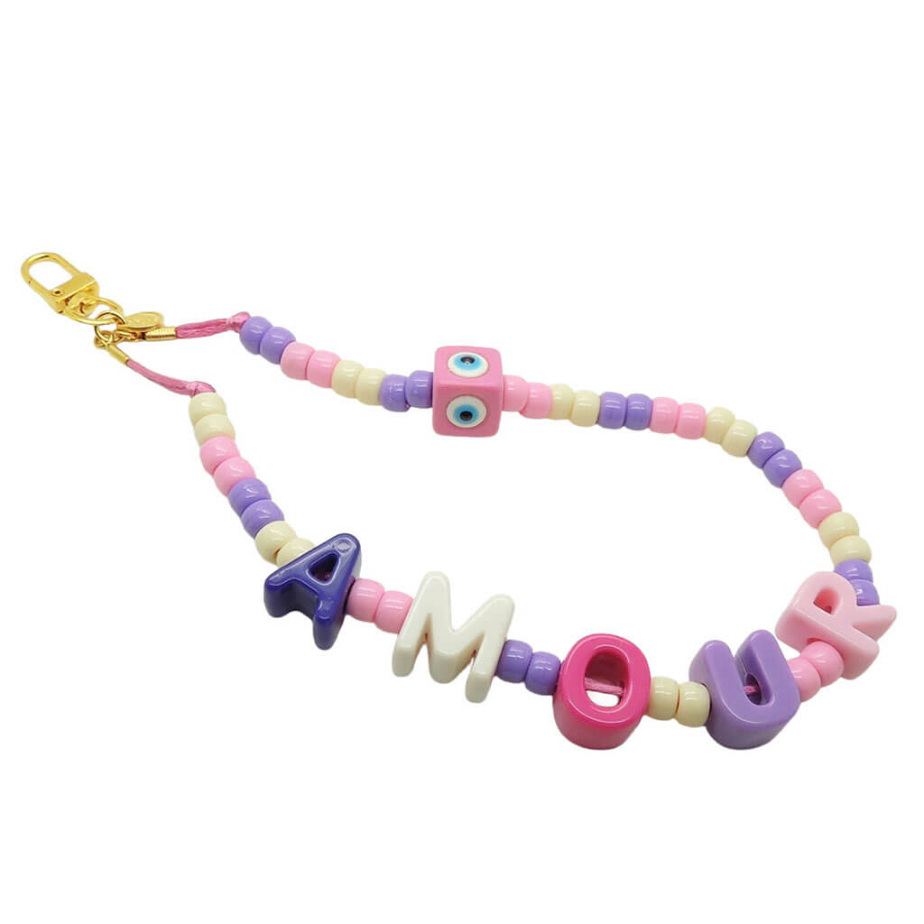 Dana Levy pastel coloured acrylic beaded phone charm strap with alphabet letters that read amour and a pastel pink evil eye cube charm with a gold clasp on a white background.