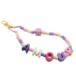 Dana Levy pastel coloured acrylic beaded phone charm strap with alphabet letters that read amour and a pastel pink evil eye cube charm with a gold clasp on a white background.