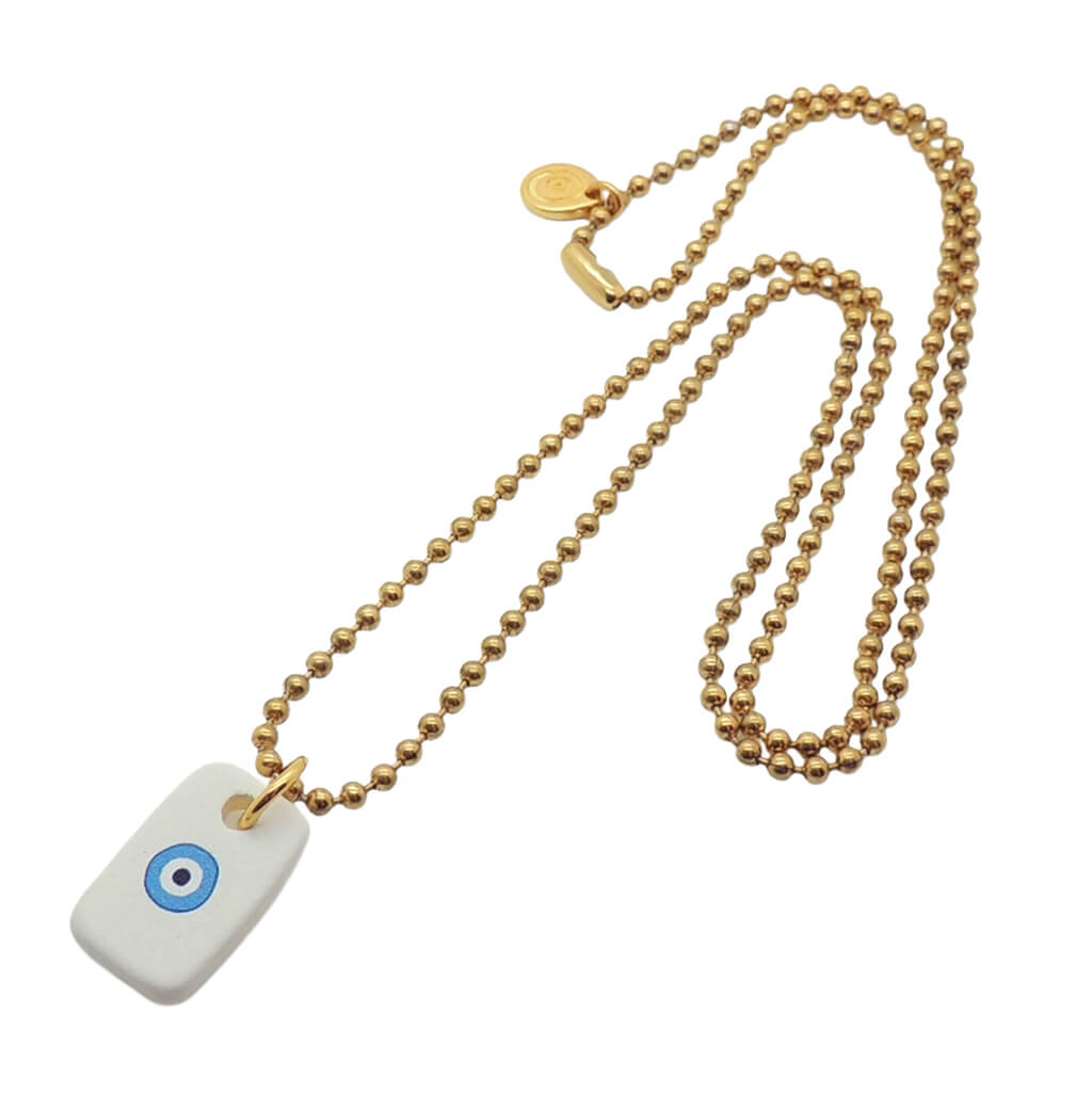 A Dana Levy men's gold plated ball chain necklace with a white ceramic dog tag with a turquoise evil eye motif on it, on a white background. 