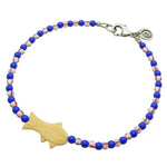 Dana Levy cream bone fish charm striped glass bead mix anklet with royal blue glass beads and white/red striped glass beads and an antique silver plated clasp on a white background. 
