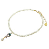 A Dana Levy white pearl beaded choker with a gold plated clasp, extender chain, and evil eye fish charm and dangly pearl, shown on a plain white background.