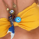 Close-up of chain necklaces with evil eye-shaped pendants and a blue enamel fish charm necklace on a yellow bikini.