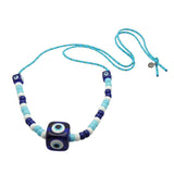 Dana Levy royal blue evil eye cube charms and turquoise white and navy glass beads on a turquoise nautical cord necklace on a white background. 