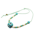 Dana Levy aqua evil eye amulet cubes and aqua, white and beige glass beads on a mint cord necklace on a white background. 