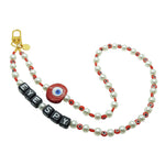 Dana Levy personalised faux pearl phone charm strap with red evil eye charm and beads and black alphabet cube 'EYE SPY' beads, with a gold plated clasp on a white background.