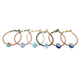 Dana Levy six braided leather cord bracelets with chunky glass evil eye amulets, displayed in a row against a plain white background. The cords are in tan brown, pink, white, and black tones, and the evil eye amulets are in various shades of blues and white.