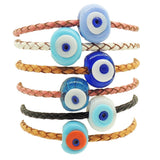 Dana Levy six braided leather cord bracelets stacked vertically, each featuring a round chunky glass evil eye bead in various colours including light blue, turquoise, royal blue, dark blue, orange, and white.
