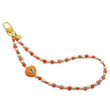 Dana Levy Glass Evil Eye Heart Faux Pearl Beaded Phone Wristlet Strap with an Orange Evil Eye Heart Charm and Evil Eye Beads on a White Background.