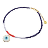 A Dana Levy glass bead choker featuring navy blue, lilac, and red beads, with a gold-tone clasp and extender chain. A round white glass evil eye pendant with a blue centre and gold bezel is attached near the front.