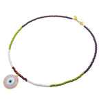 A Dana Levy glass bead necklace with purple, olive, baby pink and brown glass beads and a semi opaque pink glass evil eye pendant in the centre on a white background. 