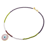 A Dana Levy glass bead necklace with purple, olive, baby pink and brown glass beads and a semi opaque pink glass evil eye pendant in the centre on a white background. 