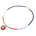 A Dana Levy beaded necklace featuring segments of navy blue, light blue, red, and green glass beads, with a red evil eye disc pendant charm and a gold clasp, shown on a plain white background.