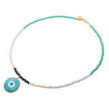 A Dana Levy glass beaded necklace with a teal evil eye pendant, featuring segments of aqua green, lilac, cream, and navy blue beads with gold plated brass hardware.
