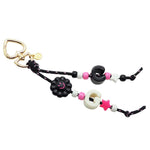 A Dana Levy maxi alphabet initial bag charm with black cords, a black smiley flower charm, C and G maxi alphabet letters and mini charms on a white background. 