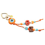 A Dana Levy maxi alphabet initial bag charm with orange cords, orange evil eye dome charm, G and Z maxi alphabet letters and mini charms on a white background. 
