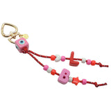 A Dana Levy maxi alphabet initial bag charm with red nautical cords, a pink evil eye cube charm, L and B maxi alphabet letters and mini charms on a white background. 