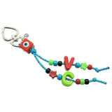 A Dana Levy maxi alphabet initial bag charm with turquoise cords, a red evil eye cube charm, V and C maxi alphabet letters and mini charms on a white background. 