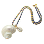 Dana Levy large spiral seashell charm with a small cowrie shell charm on a pink yellow and blue braid cord necklace diagonal flat lay on a white background. 