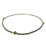 Grey glass beaded necklace with gold skull charms on a white background by Dana Levy 