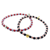 Dana Levy set of heart charm glass beaded bracelets with red, white and blue stripe and black with red striped beads on a white background.