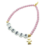 A Dana Levy light pink newborn baby milestone glass bead bracelet with birth date in acrylic letters and a gold plated mini girl icon charm, on a white background. 