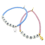 a pair of Dana Levy blue and pink glass bead bracelets with milestone dates in acrylic letters and mini boy and girl icon charms, on a white background. 