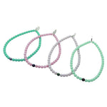 Dana Levy Set of four glass beaded bracelets in green, pink, grey, and light mint green on a white background