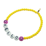 Dana Levy personalised name glass bead bracelet with hello in white acrylic letters, pink smiley charms and yellow glass beads, on a white background. 
