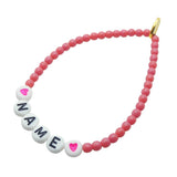Dana Levy personalised name glass bead bracelet with name in white acrylic letters, pink hearts and dark rose glass beads, on a white background. 