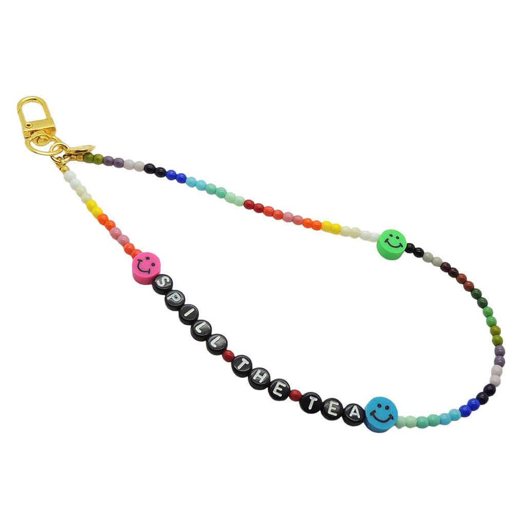 Dana Levy rainbow coloured glass bead phone charm strap with 'SPILL THE TEA' in black acrylic beads and multicoloured smiley face charms on a white background