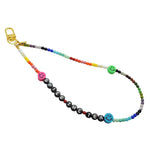 Dana Levy rainbow coloured glass bead phone charm strap with 'SPILL THE TEA' in black acrylic beads and multicoloured smiley face charms on a white background