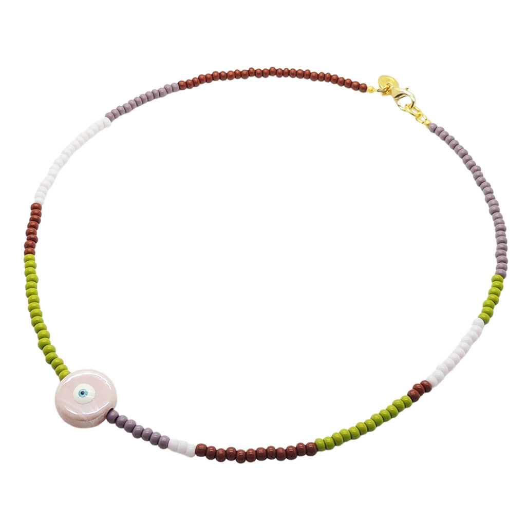 A Dana Levy beaded necklace with a gradient of colours including brown, lilac, purple, and green, featuring a central round light pink ceramic evil eye bead and a gold clasp, shown on a plain white background.