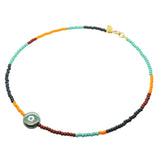 A glass bead necklace by Dana Levy with segments of aqua, forest green, orange, and brown beads, featuring a round ceramic pearlised forest green and white evil eye charm and a gold clasp, shown on a plain white background.