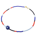 A Dana Levy glass bead necklace with a mix of royal blue, red, light blue and black glass beads, and a large blue ceramic evil eye disc pendant in the centre, on a white background. 