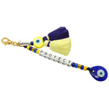 Dana Levy Personalised Alphabet Cube Evil Eye Charm Tassel Keyring - A Gold Plated Keyring with Protect Spelled Out in White Alphabet Letter Cube Beads, with Yellow and Royal Blue Evil Eye Amulets and a Baby Yellow and Indigo Double Tassel.