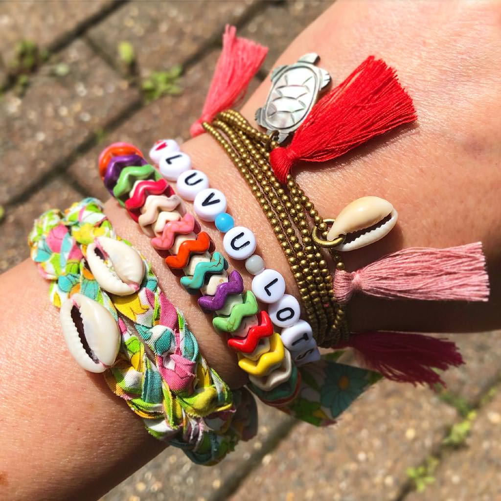 Dana Levy personalised name bracelet that reads luv you lots with friendship bracelets on a wrist at Glastonbury.