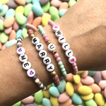 Dana Levy personalised name glass bead bracelets spelling out "Will You Marry Me?" in a variety of pastel colours worn on a wrist with a wedding almond dragee background. 