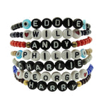 Dana Levy personalised name glass bead bracelets in a stack in a variety of bead colours with a variety of boys names and charm on a white background.