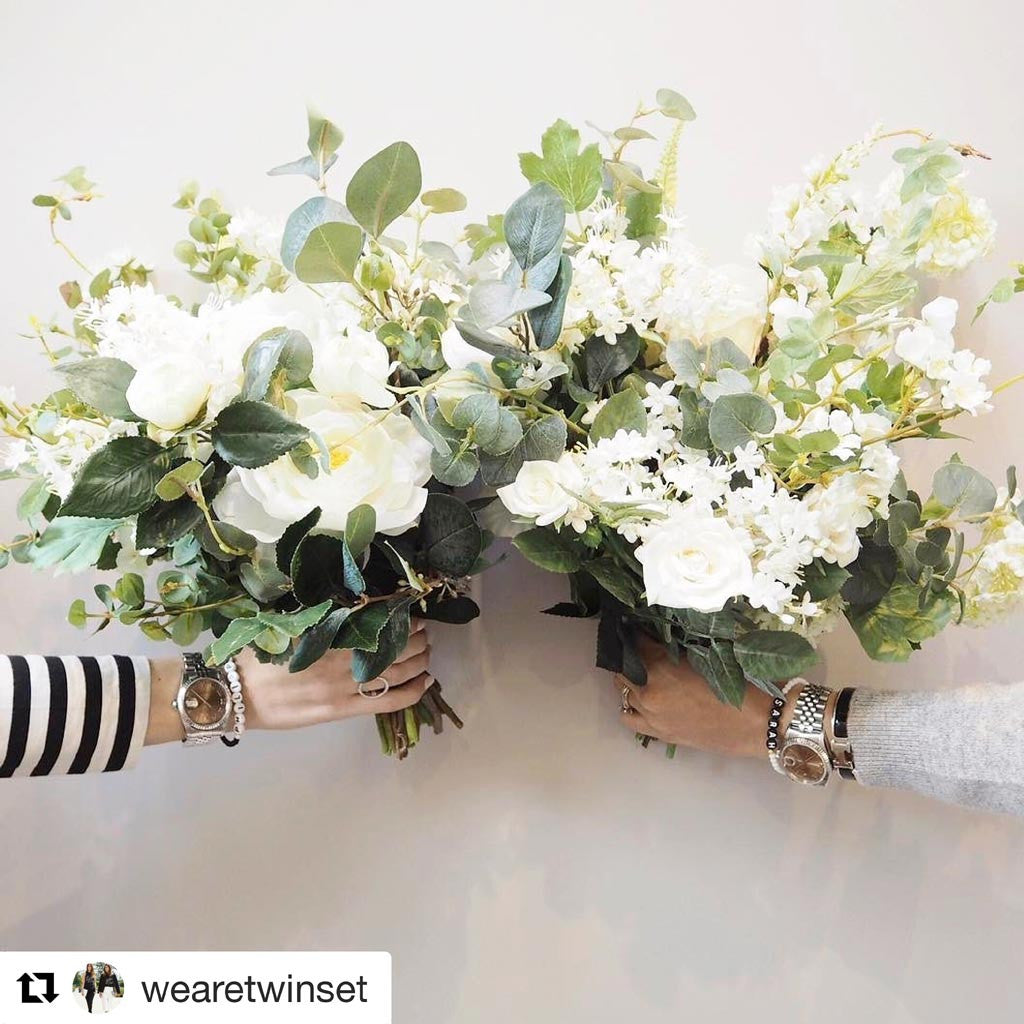 Dana Levy personalised name glass bead bracelets worn by We are Twinset's Sarah and Philippa, with bunches of flowers in their hands in front of a white wall. 