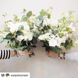Dana Levy personalised name glass bead bracelets worn by We are Twinset's Sarah and Philippa, with bunches of flowers in their hands in front of a white wall. 