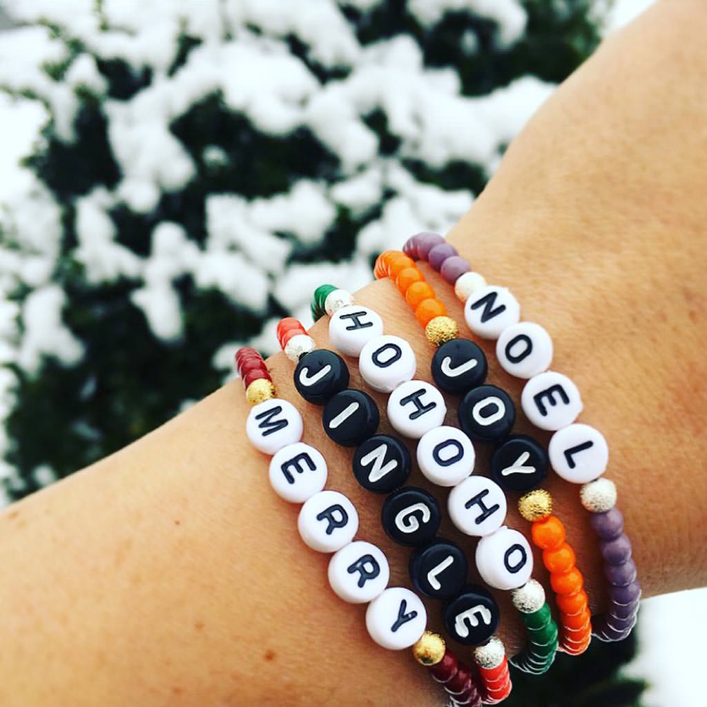 Dana Levy Christmas themed personalised name glass bead bracelets stack reading Noel Joy Hohoho Jingle and Merry, in the snow. 