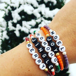 Dana Levy Christmas themed personalised name glass bead bracelets stack reading Noel Joy Hohoho Jingle and Merry, in the snow. 